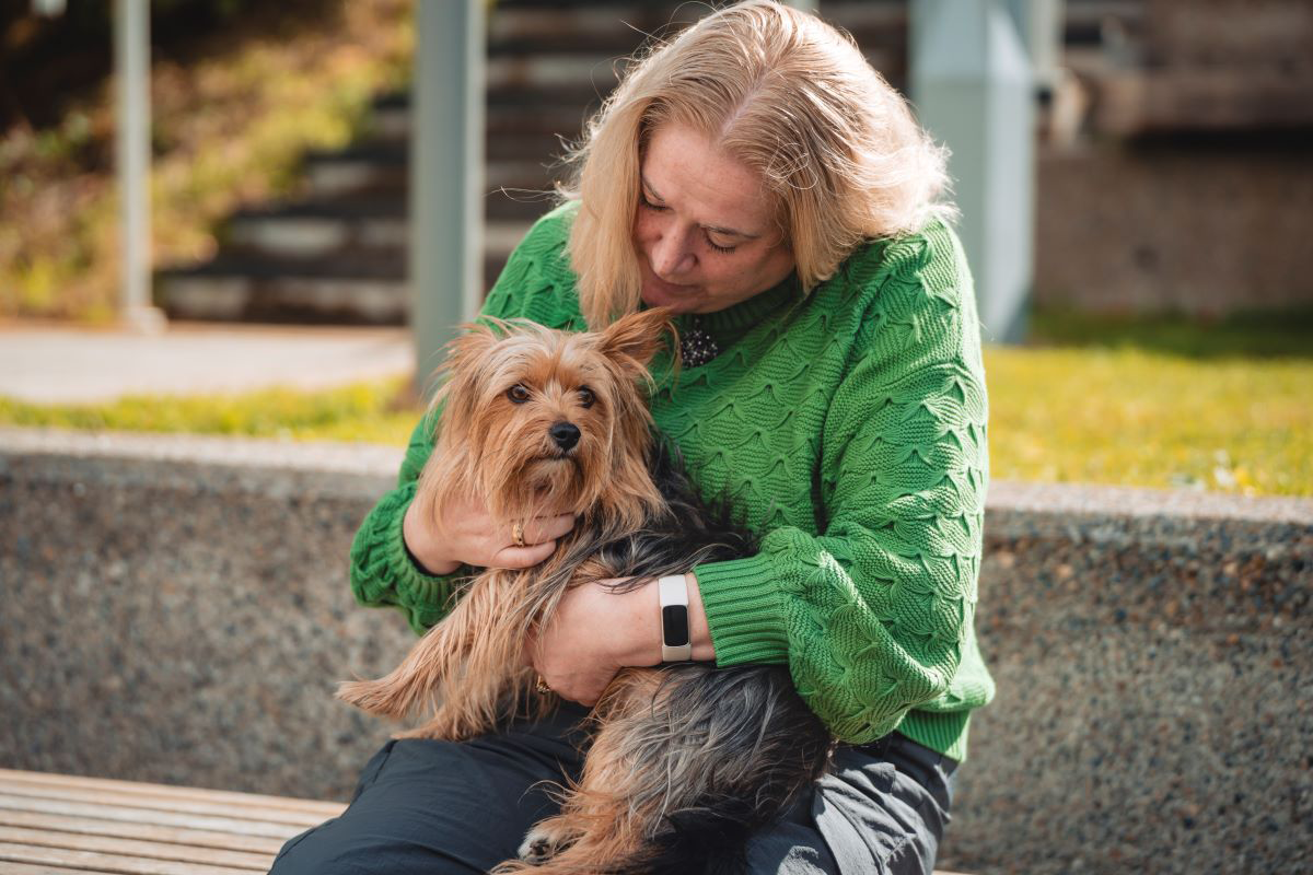 Person in green sweater holding a small dog on a bench.