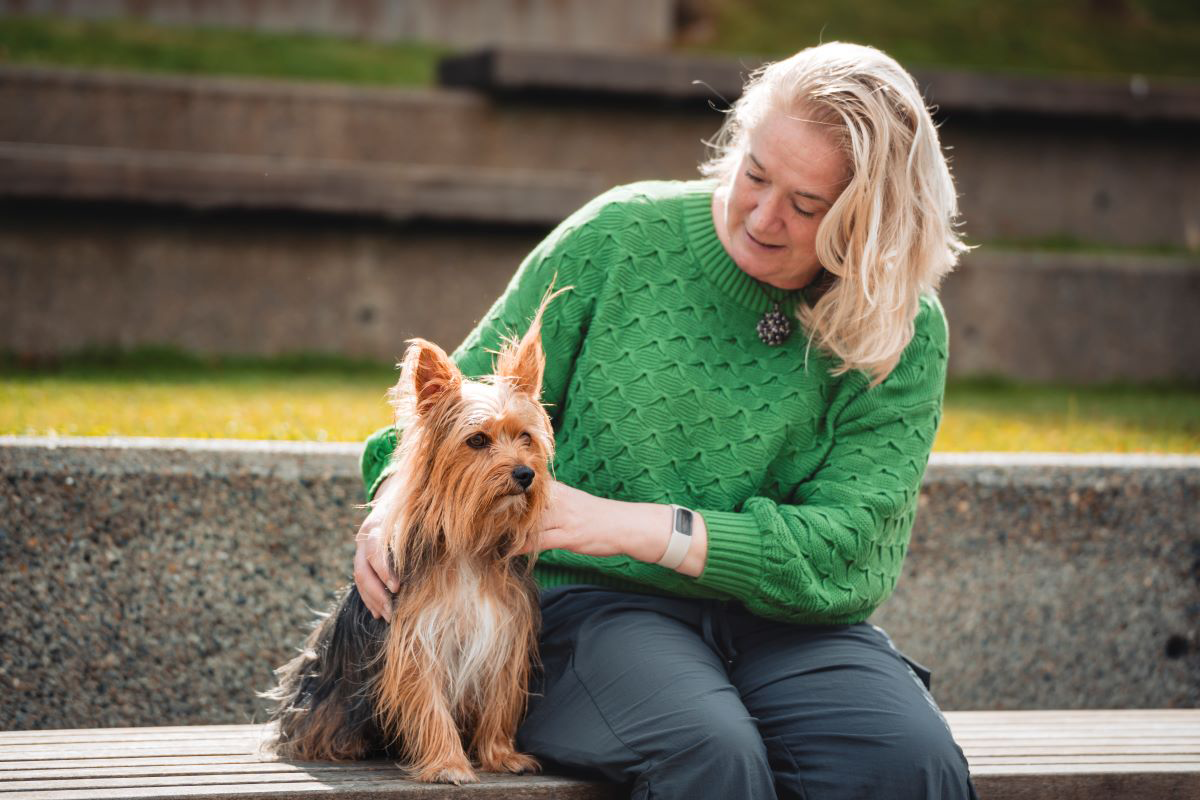 Woman in green sweater sitting with a small dog on a bench.