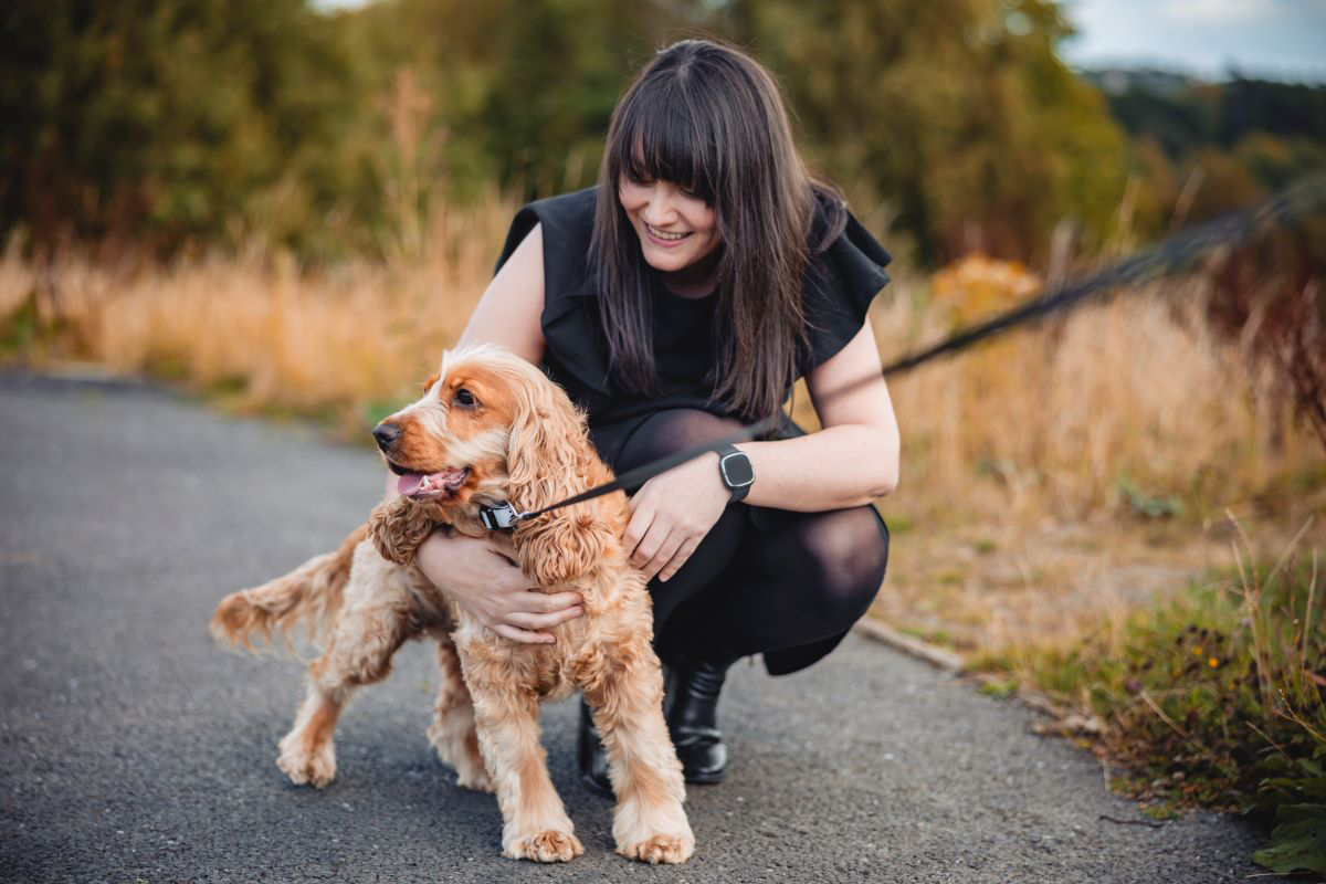 Woman crouching and hugging a brown dog on a path.