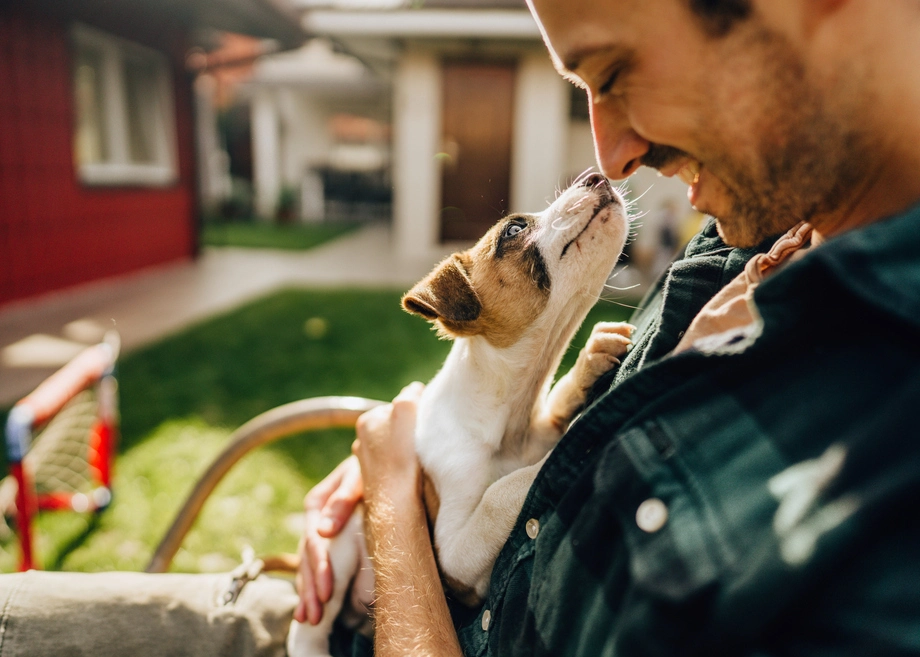 Man smiling at puppy in his arms outdoors.